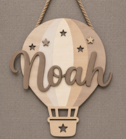 Personalized wooden hot air balloon wall hanging with the name 'Noah' in script, hanging against a textured linen background.